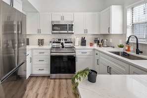 A modern kitchen with white cabinets, stainless steel appliances, and a wooden floor.