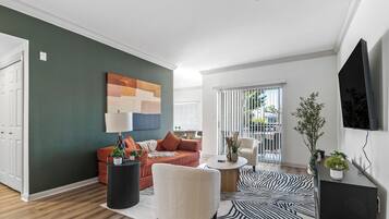 Een moderne woonkamer met een bank, fauteuil en een flatscreen televisie aan de muur.