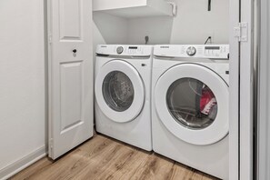 A laundry room with two front-loading washing machines, a white door, and a wooden floor.