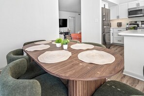 A modern kitchen with white cabinets, stainless steel appliances, and a dining area with a wooden table and green upholstered chairs.