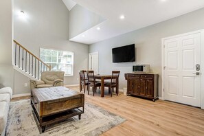 A spacious living room with a high ceiling, a wooden dining table, a sofa, and a flat-screen TV mounted on the wall. - Ponderosa Estate! Sleeps 18 w/ Hot Tub by USAFA (Monument)