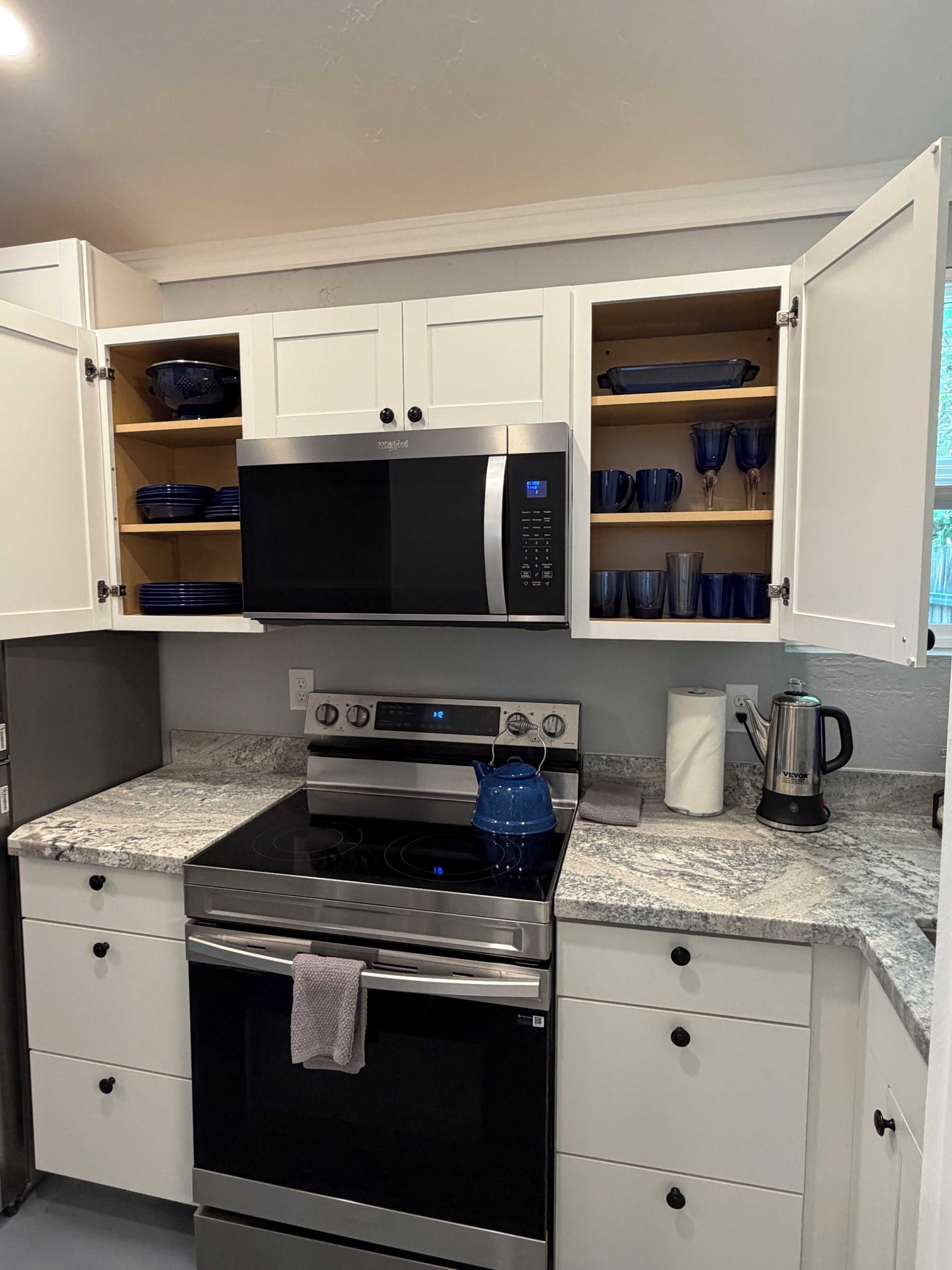 A kitchen with a built-in microwave, oven, and a kettle on the countertop.