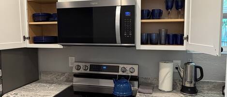 A kitchen with a built-in microwave, oven, and a kettle on the countertop.