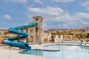 A swimming pool with a blue water slide, a tower structure, and a view of houses in the background.
