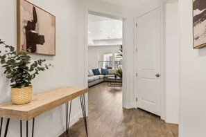 Ein Flur mit einer Holzbank, einem Blumentopf und einer Tür zu einem Wohnbereich mit Sofa und Couchtisch.