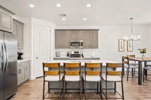 A modern kitchen with a central island, stainless steel appliances, and wooden chairs.