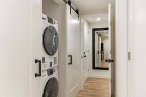 A laundry room with a front-loading washer and dryer, a sliding door, and a hallway leading to another room. - Fallridge Condo - Steps to Nordic Center and Bus (Vail)