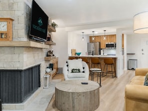 A modern living room with a fireplace, a TV mounted on the wall, a round coffee table, and a comfortable sofa. - Fallridge Condo - Steps to Nordic Center and Bus (Vail)
