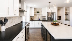 A modern kitchen with white cabinetry, stainless steel appliances, and a central island with a bowl and plant. - 6 bdrm 5bath in Old Town with Casita, Game Room, and Pool. Two Kitchens!  (Scottsdale)