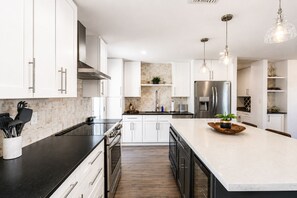 Een moderne keuken met witte kasten, roestvrijstalen apparatuur en een centraal eiland met een kom en plant.