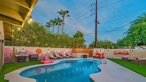 Piscina externa com espreguiçadeiras, área de churrasco e parede decorativa com um mural de pôr do sol.