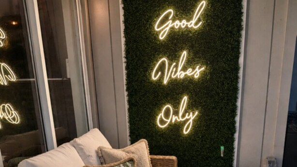 A cozy seating area with a wicker sofa, a wall-mounted neon sign, and a small table with drinks and a candle. - 6 bdrm 5bath in Old Town with Casita, Game Room, and Pool. Two Kitchens!  (Scottsdale)
