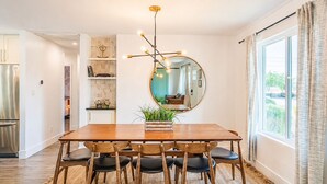Uma sala de jantar com uma mesa de madeira, cadeiras, um espelho e uma luminária moderna.