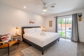 A bedroom with a bed, bedside lamps, a chair, a desk, a ceiling fan, and a view of an outdoor pool area. - 6 bdrm/ 5bdrm in Old Town Scottsdale with Casita, Game Room, and Pool! (Scottsdale)
