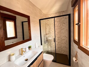 Casa de banho com lavatório branco, espelho, sanita e cabine de duche com parede de vidro.