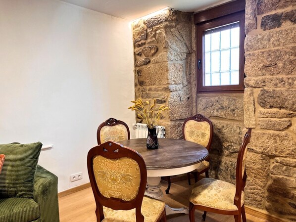 A dining area with a stone wall, a round table, four chairs, and a vase with dried plants.