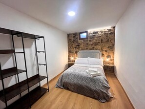 A bedroom with a bed, a TV mounted on a stone wall, and a wooden shelf unit.