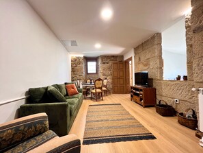 A cozy living room with a stone wall, a green sofa, a wooden coffee table, and a television.