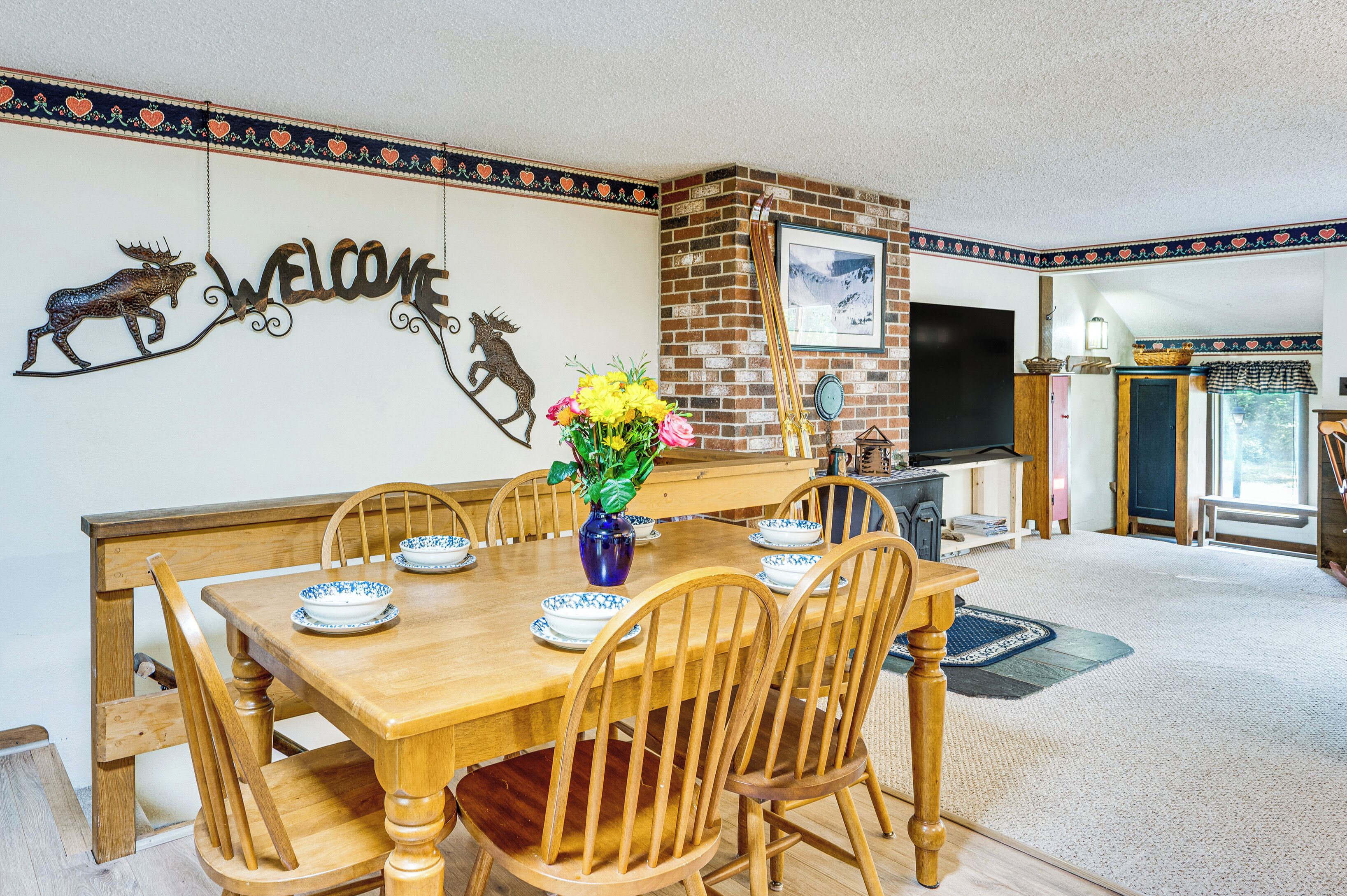 A dining area with a wooden table and chairs, a vase with flowers, and a 'WELCOME' sign with animal decorations.