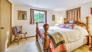 Ein Schlafzimmer mit einem hölzernen Himmelbett, einem kleinen Stuhl, einem Fenster mit Vorhängen und einem wandmontierten Spiegel.