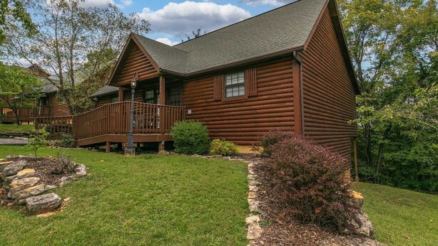 A log cabin with a porch, surrounded by a well-maintained lawn and a stone border.