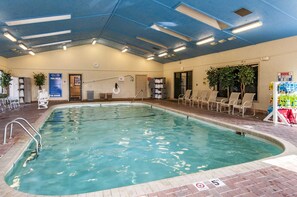 An indoor swimming pool with a no diving sign, lounge chairs, and a lifeguard warning sign.
