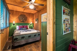 A cozy room with a bed, a ceiling fan, wooden walls, and a poster on the wall. - Resort Cabin! Whirpool Tub, Lots of Space, Sleeps 8! | 9 (Branson)