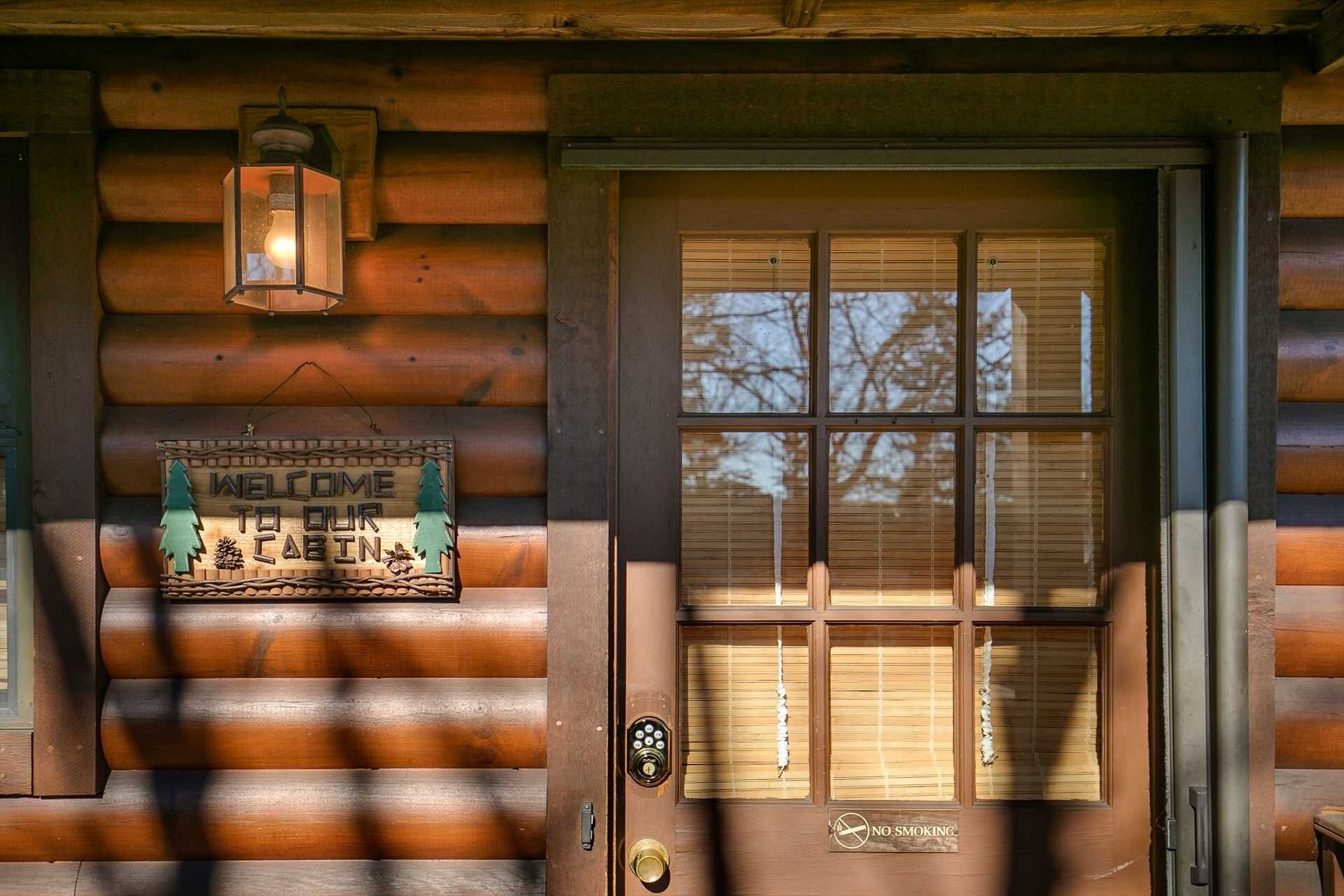 A wooden cabin entrance with a welcome sign, a door with a window, and a no-smoking sign.