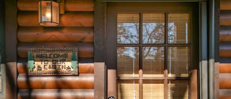 A wooden cabin entrance with a welcome sign, a door with a window, and a no-smoking sign.