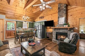 Interior de una cabaña de troncos con comedor, cocina, chimenea y una zona de estar acogedora.
