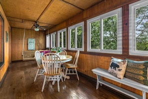 A wooden interior with a dining area, a bench with a bear pillow, and large windows. - Resort Cabin! Whirpool Tub, Lots of Space, Sleeps 8! | 9 (Branson)