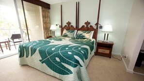 Une chambre d’hôtel avec un grand lit, deux lampes de chevet, une tête de lit en bois et une vue sur l’extérieur, accessible par une porte-fenêtre coulissante.