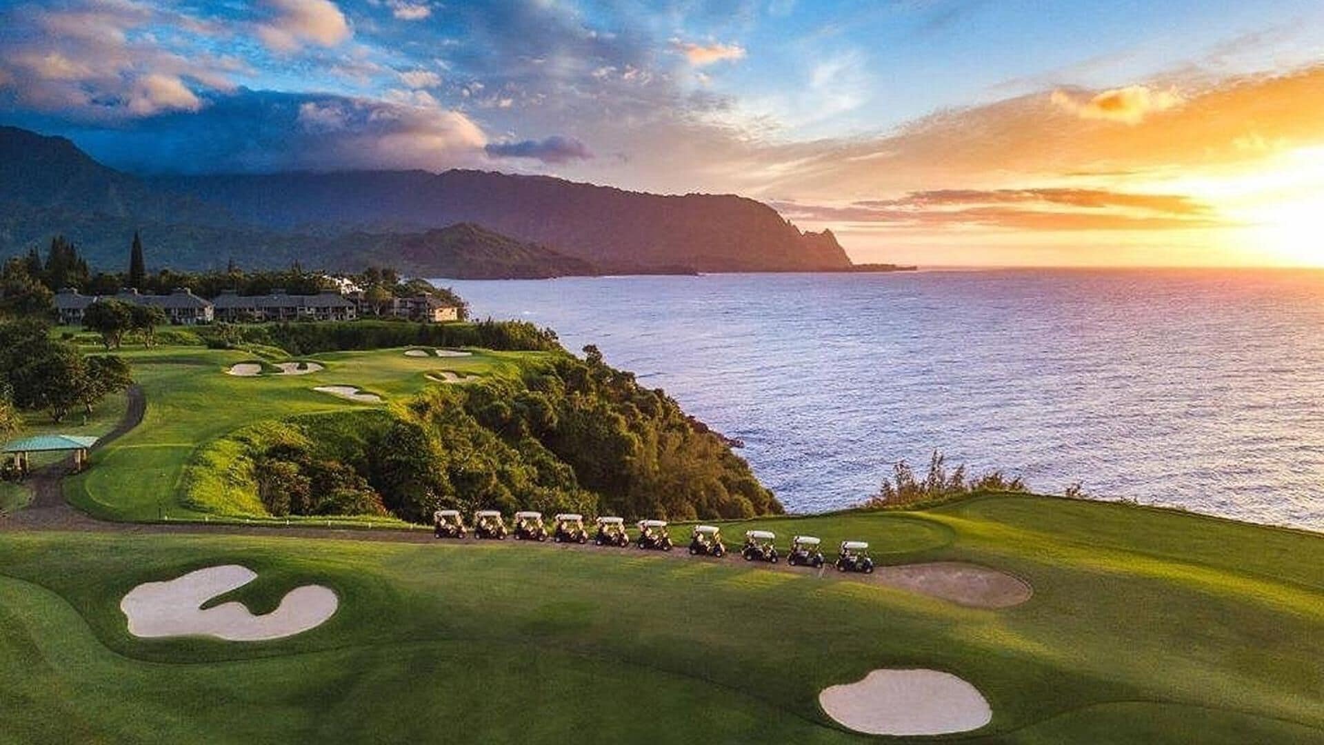 Een golfbaan met bunkers en uitzicht op de oceaan bij zonsondergang.
