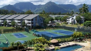 A tennis court complex with multiple courts, surrounded by buildings and a mountain backdrop. - Princeville North Shore Escape - The Cliffs Club 1BR Suite, Ocean Area (Princeville)