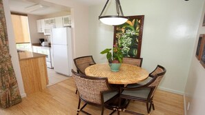 Un coin repas avec une table ronde, des chaises en osier, une plante en pot et un luminaire suspendu.