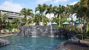 Une piscine agrémentée d’une cascade, entourée de palmiers et de chaises longues.