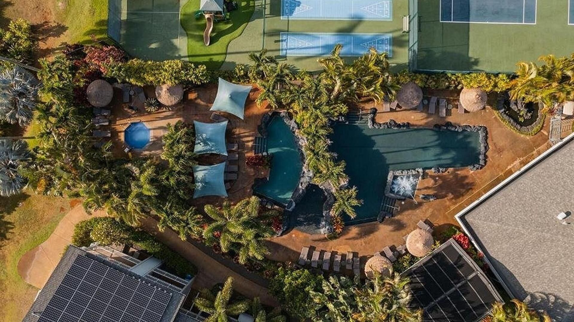 Oversigtsbillede af et resort med flere swimmingpools, palmer og solpaneler.