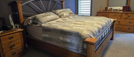A bedroom with a wooden bed, a nightstand, a dresser, a mirror, and a window with blinds.