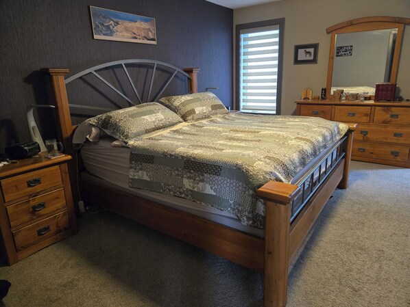 A bedroom with a wooden bed, a nightstand, a dresser, a mirror, and a window with blinds.