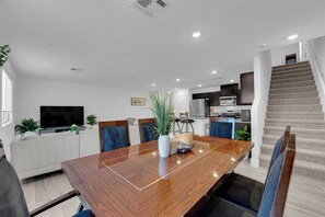 Un salon moderne avec une table à manger en bois, un téléviseur à écran plat et un escalier menant à l’étage supérieur.