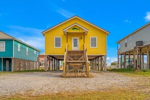 Une maison jaune avec un escalier en bois menant à l’entrée, entourée d’autres maisons.
