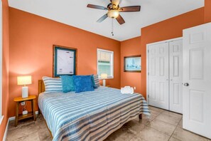 Une chambre à coucher avec un lit, deux tables de chevet, un ventilateur de plafond et une porte.