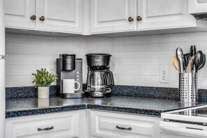 A kitchen with white cabinets, a coffee maker, a kettle, and a plant on the counter. - Mellow Yellow · New! Bay & Gulf Views, Steps to Beach, Sleeps 8 (Gulf Shores)