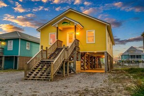 A yellow building with a staircase leading to a porch, surrounded by other buildings. - Mellow Yellow · New! Bay & Gulf Views, Steps to Beach, Sleeps 8 (Gulf Shores)