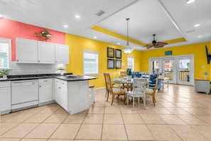 A kitchen with white cabinets, a dining area with a table and chairs, and a ceiling fan. - Mellow Yellow · New! Bay & Gulf Views, Steps to Beach, Sleeps 8 (Gulf Shores)