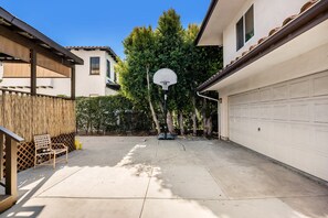 A residential backyard with a basketball hoop, a wooden bench, and a thatched wall. - Spanish Gem in West Hollywood (Los Angeles)