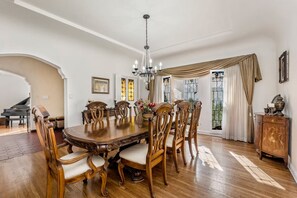 A dining room with a large wooden table, ornate chairs, a chandelier, and a piano in the background. - Spanish Gem in West Hollywood (Los Angeles)