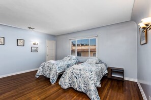 A bedroom with two beds, a window with blinds, a door, and wall-mounted artwork. - Spanish Gem in West Hollywood (Los Angeles)