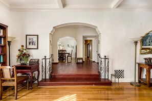 A spacious living room with a wooden staircase, a bookshelf, and a dining area in the background. - Spanish Gem in West Hollywood (Los Angeles)