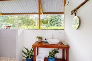 Une petite salle de bain avec une table en bois, un lavabo blanc et une fenêtre donnant sur un paysage verdoyant.